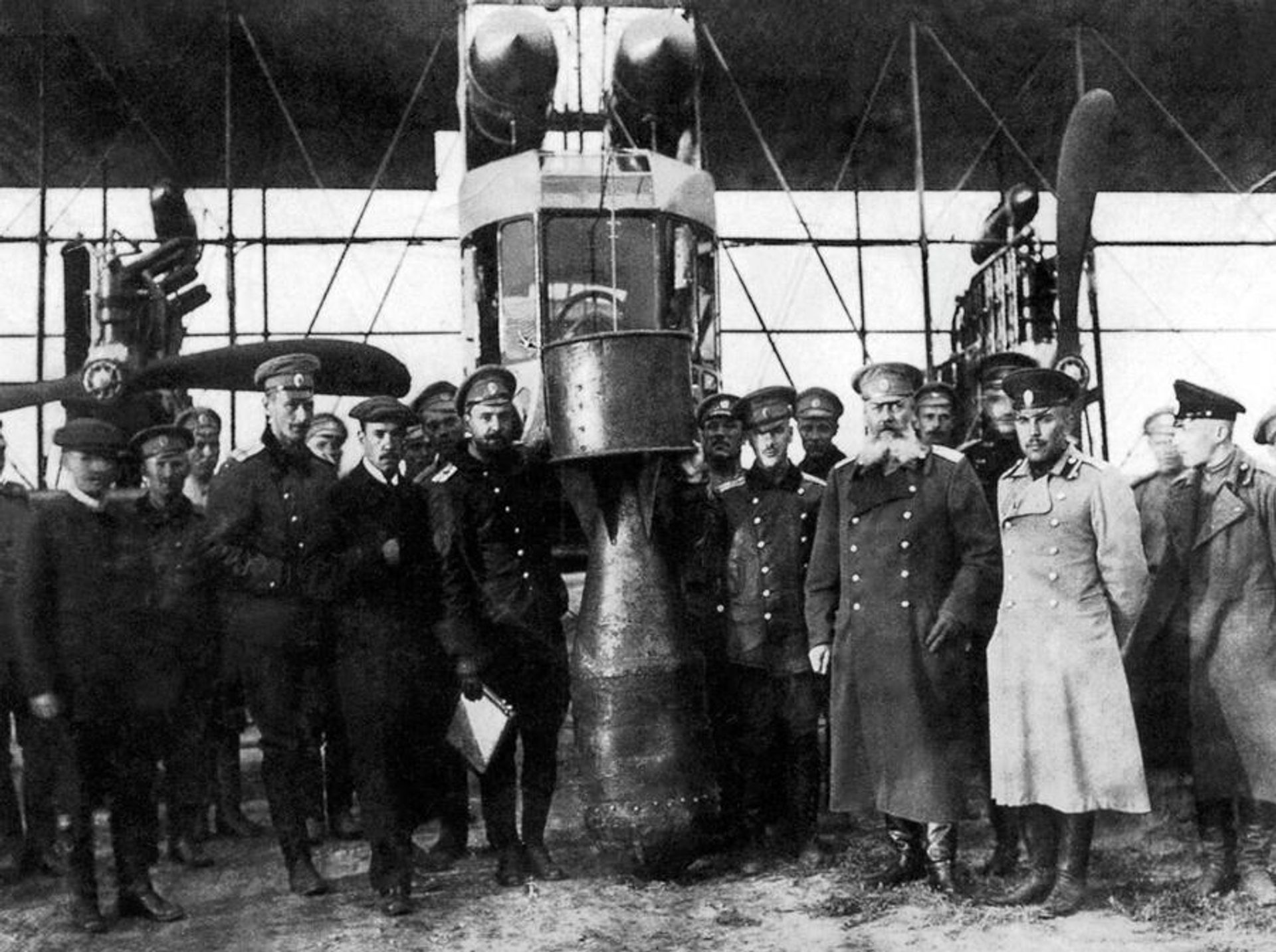 Игорь Сикорский (третий слева, в кепке), Михаил Шидловский (третий справа, в бороде) и 25-пудовая/400 кг. учебная бомба (в центре)  - РИА Новости, 1920, 18.06.2026