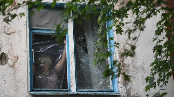 Женщина затягивает полиэтиленовой пленкой окно, разбитое в результате обстрелов ВСУ Донецка